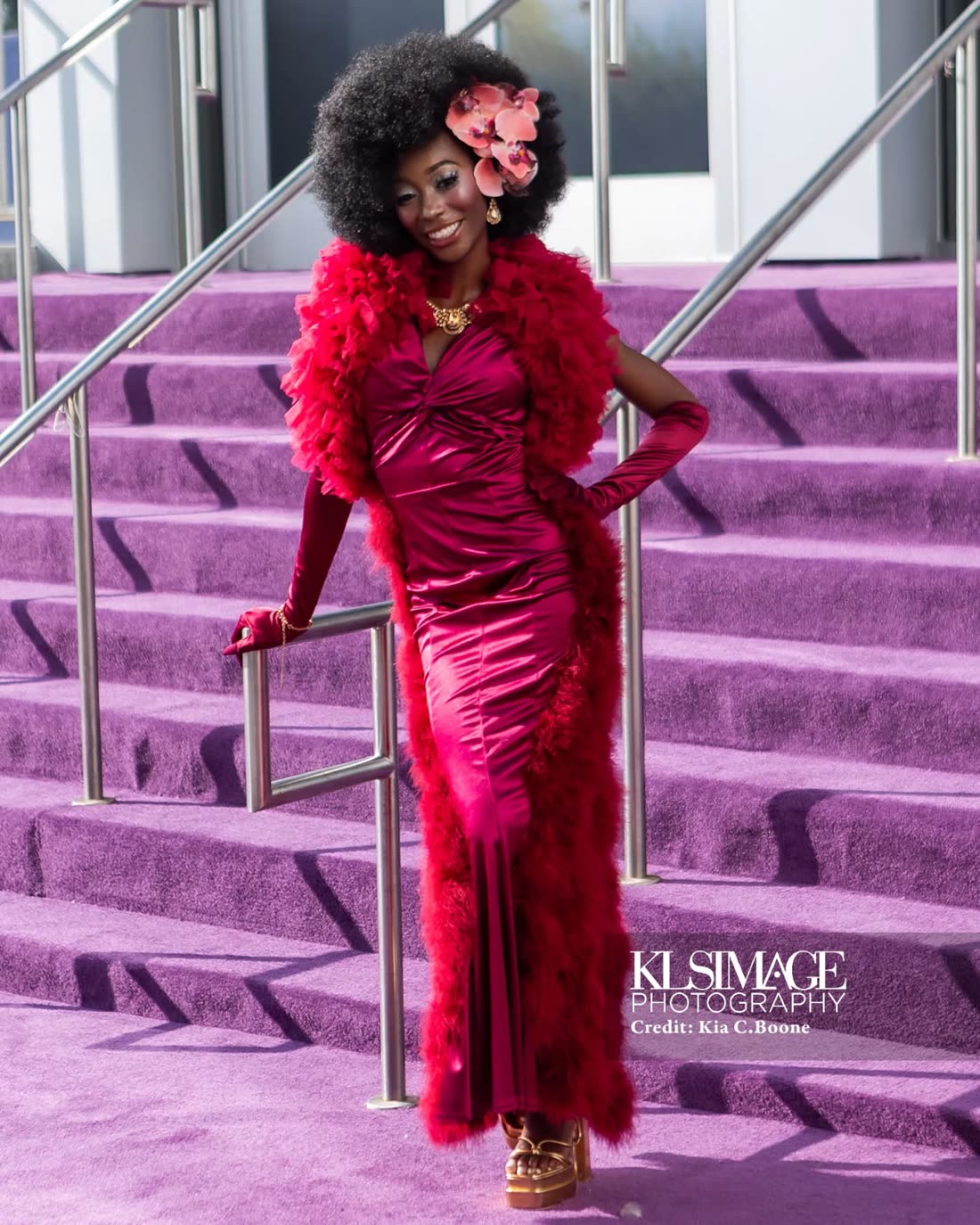 Red feather-trimmed gown, hand on the railing